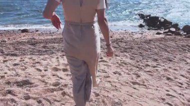 Kayalık bir kıyı şeridinde duran genç bir kadın, kollarını gökyüzüne doğru uzatarak rahatlama ve özgürlük jesti yapıyor..