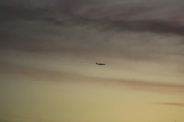 Avião no céu com nuvens pôr do sol cores da noite — Fotografia de Stock