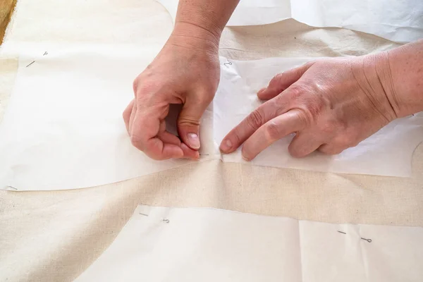 Tailors's hand fixes paper cutting layouts of dress to calico cloth by pins on wooden table at home — Stock Image Tailors Hand Fixes Paper Cutting Layouts Dress Calico Cloth Pins Royalty Free Stock Images