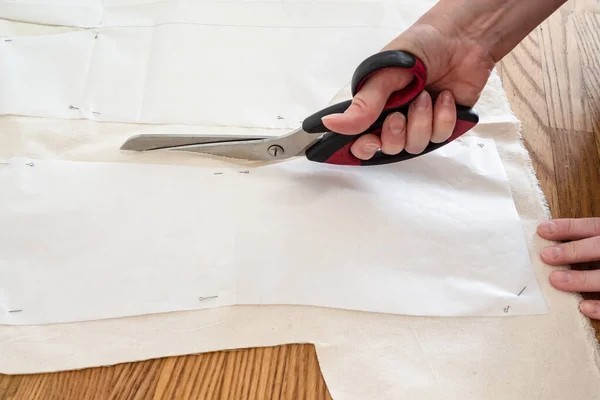 Hand cuts mock-up fabric by scissors according with pattern layouts of dress on wooden table at home — Stock Image Hand Cuts Mock Fabric Scissors According Pattern Layouts Dress Wooden Stock Image
