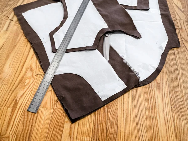 Steel rule lays on a layout of sewing patterns of dress on brown fabric on wooden table at home — Stock Image Steel Rule Lays Layout Sewing Patterns Dress Brown Fabric Wooden Stock Photo