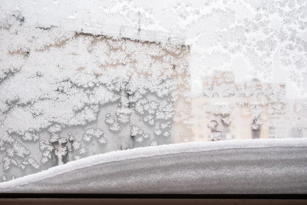 snowbank on window frame and frozen glass at home in urban house on overcast winter day (focus on the surface on windowpane)
