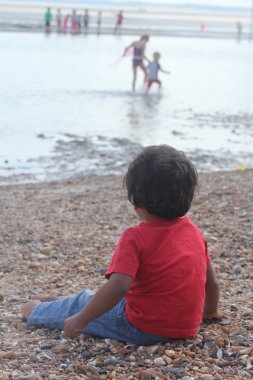 Genç Hintli yürümeye başlayan çocuk çocuk iskambil kum kıyı ve deniz okyanus plaj sahil oynayan diğer çocuklar izliyor. sevimli küçük çocuk deniz kıyıya yakın yerde oynamak.