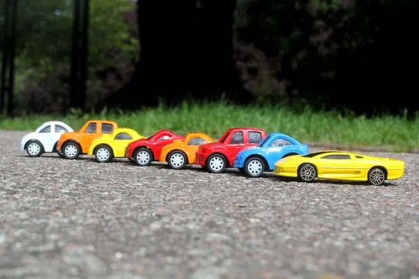 Minature carros coloridos de pé em linha no conceito de venda de estradas. Diferentes carros coloridos - azul, amarelo, laranja, carros de cor branca e vermelha de pé lado a lado na estrada ao lado da grama — Fotografia de Stock