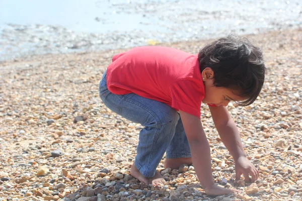 Jovem menino criança indiana brincando em pedra de areia perto da costa da praia do mar oceano. bonito criança pequena jogar perto da costa do mar . — Fotografia de Stock