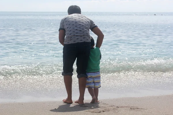 Indian father and son playing in the calm ocean sea water waves on a sunny summer with blue sky in the background