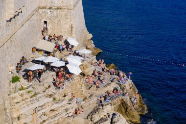 Hırvatistan 'ın eski Dubrovnik kentindeki uçurum kenarındaki barın manzarasının keyfini çıkaran insanlar