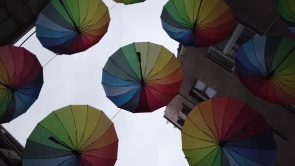 Wiele kolorowych tęczy otwarte parasole wiszą nad wąską uliczką między domami. — Wideo stockowe