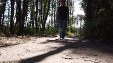 Ormanda yürüyen orta yaşlı bir adam. Günlük kıyafetli bir adam orman yolunda yürüyor.