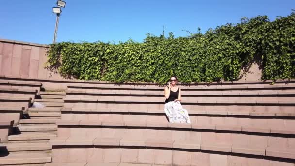 Καλοκαίρι ηλιόλουστη μέρα. Μπλε φωτεινό ουρανό. Πράσινα φύλλα. πέτρα αμφιθέατρο στο πάρκο της πόλης — Αρχείο Βίντεο
