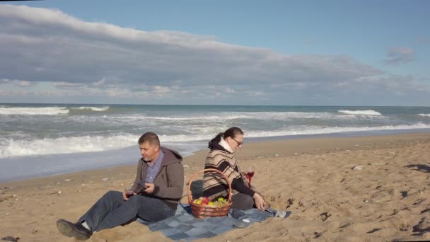 Man, vrouw zit op het strand met hun rug naar elkaar, kijkend naar hun telefoons — Stockvideo