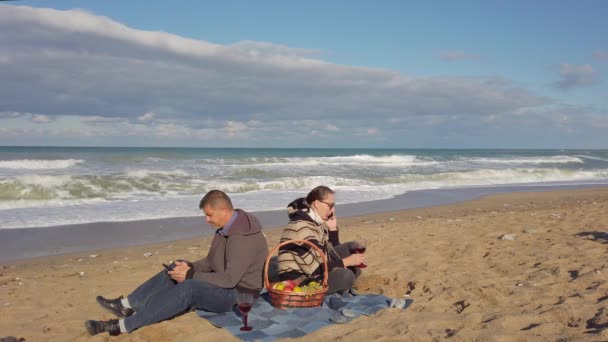 Man, vrouw zit op het strand met hun rug naar elkaar, kijkend naar hun telefoons — Stockvideo