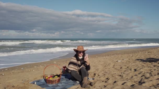 Mujer joven se sienta en la playa de arena en la manta. Chica morena hablando por teléfono celular — Vídeo de stock