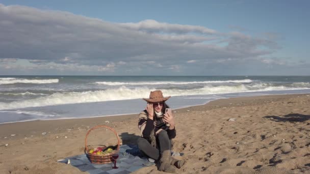 Mujer joven se sienta en la playa de arena en la manta. Chica morena hablando por teléfono celular — Vídeos de Stock