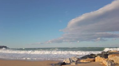 Taştan dalgalar. Kumsalda. Mavi gökyüzü. Beyaz köpüklü büyük deniz dalgaları