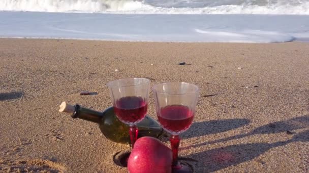 Δύο κρυστάλλινα ποτήρια με κόκκινο κρασί πάνω στην άμμο. γυάλινο μπουκάλι κρασί. Κόκκινο μήλο — Αρχείο Βίντεο
