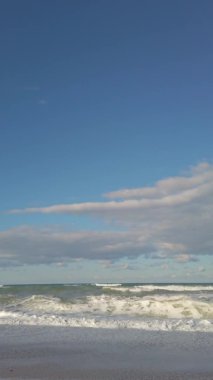 Dikey çekim. Kumsalda. Mavi gökyüzü. Deniz dalgaları, beyaz köpük. Sahilde tatil.