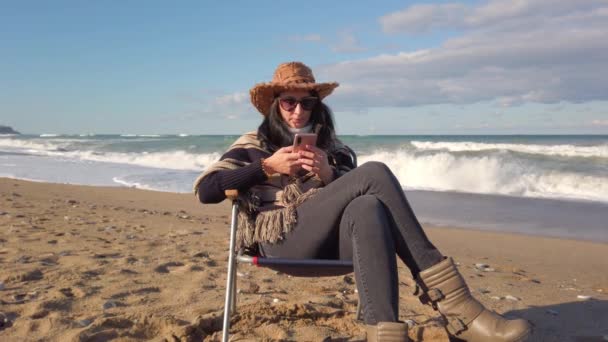 Chica morena hablando por teléfono celular. mujer con el pelo oscuro se sienta en la playa de arena — Vídeo de stock