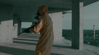 Gaz maskeli, koruyucu giysili, silahlı bir adam tamamlanmamış binada yürüyor..