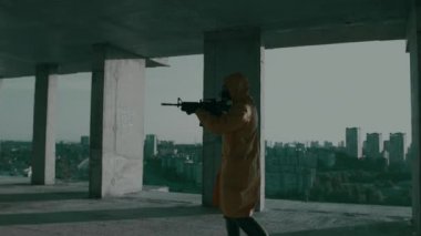 Koruyucu giysili, gaz maskeli, silahlı bir adam bitmemiş bir ofiste yürüyor.