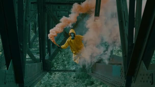 Homem de terno protetor e máscara de gás está sob ponte, brandindo bomba de fumaça. — Vídeo de Stock