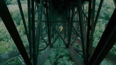 Koruyucu giysili ve gaz maskeli adam köprünün altında duruyor ve elinde sis bombası sallıyor..