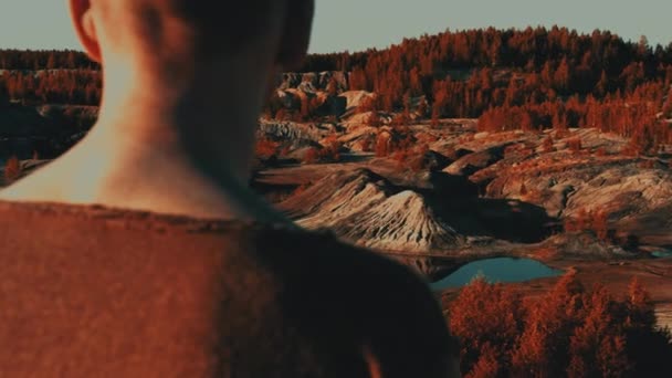 Człowiek stoi z bliska na wzgórzu i patrzy na pagórkowatą dolinę podobną do marsjańskiej. — Wideo stockowe