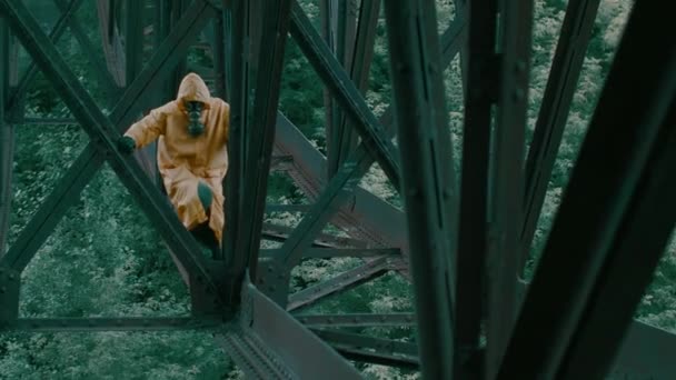 Man in protective suit, gas mask walks over an iron bridge over the abyss. — Stock Video