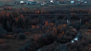 Nehrin karşısındaki eski bir viyadük demiryolu yakınlarındaki bir sonbahar ormanının arka planına karşı.. 