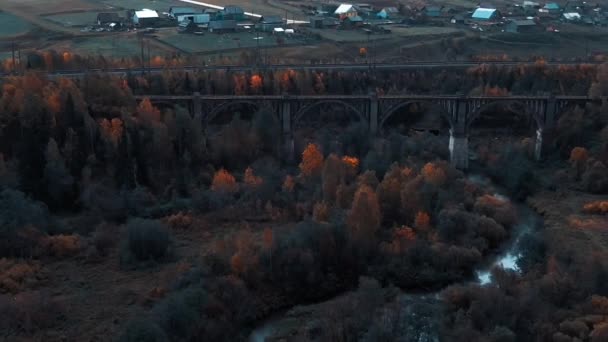 Um velho viaduto através do rio contra o pano de fundo de uma floresta de outono perto da ferrovia. — Vídeo de Stock