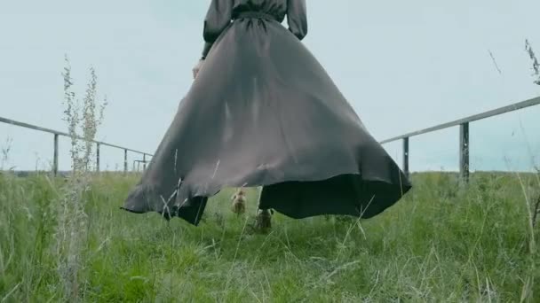 Chica en vestido de noche negro que fluye en el viento, zapatos caminando sobre la hierba verde. — Vídeos de Stock