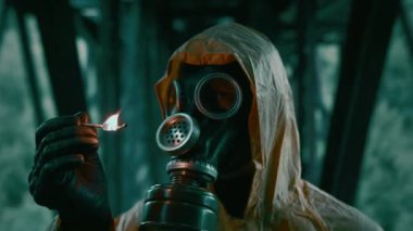 Koruyucu kıyafetli, gaz maskeli bir adam kibrit yakıyor, etrafa bakıyor..