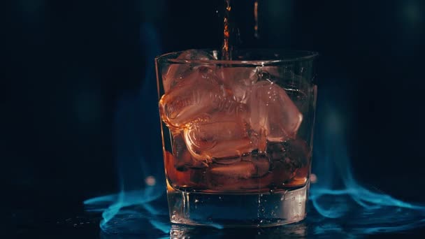 Ουίσκι χύνεται σε ένα ποτήρι πάγο, ουίσκι πιτσιλίζει στο μπαρ ενάντια, μπλε φλόγες — Αρχείο Βίντεο