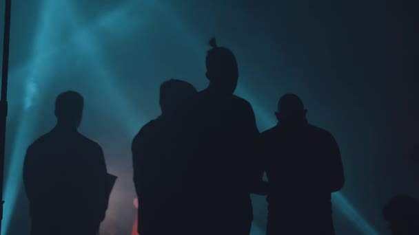 Dunkle Silhouetten von Männern von hinten in einem dunklen Hangar, der von blauen Strahlen beleuchtet wird. — Stockvideo
