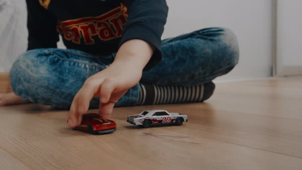 Niño en jeans y se sienta en el suelo con las piernas cruzadas, juega con la máquina. — Vídeos de Stock