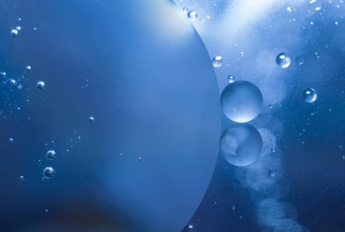 Suyun içinde renkli yağ damlaları olan soyut bir arka plan. Psikedelik desen görüntüsü. Bulanık mavi arkaplanda küreler. Sudaki yağ damlaları ve gölgeler.