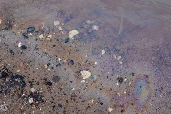 Gasolin stains in a muddy puddle on the road side. Oil spill. Environment pollution.