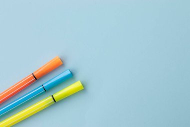 Açık mavi arka planda sarı, turuncu ve mavi keçeli kalemler. Kopyalama alanı olan düz bir üst görünüm.