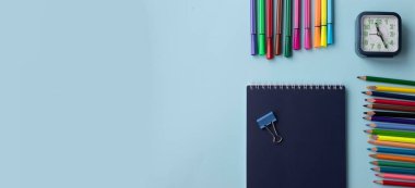 Mavi arka planda okul ve ofis malzemeleri: kalem, ataç, not kağıdı, renkli kalemler, renkli kalemler, keçeli kalemler ve çalar saat. Konsept: okula geri dönmek. Flatlay, üst görünüm.