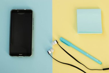 Mavi ve sarı arka planda not defteri, cep telefonu, kalem ve kulaklık olan minimum okul malzemeleri. Okula dönmek ya da yeni gerçeklikte çevrimiçi eğitim almak için kopya alanı olan daire.