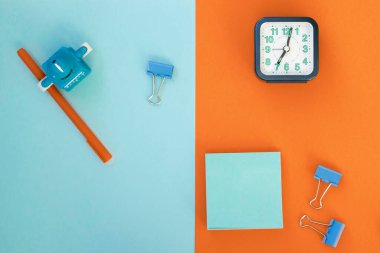 Açık mavi (turkuaz) ve turuncu arka plan üzerine en az okul ve ofis malzemesi: kalem, ataç, not kağıdı, alarm. Konsept: okula geri dönmek. Düz çizgi, üst görünüm, uzun pankart.