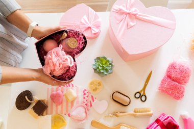 Doğal vücut bakımı, banyo malzemeleri, el yapımı sabun, banyo bombası, ahşap fırça, sünger taşı, sünger taşı, havlu ve dekoratif ayıyla seti hazırlayan bir kadın..