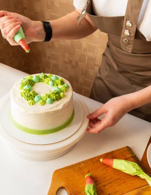 Yeşil kremalı krema koymak ve evde doğum günü pastası süslemek için şekerleme torbası kullanan bir kadın. Ev yapımı yemek pişirme ve pasta süsleme kavramı. Pasta yapan kadın pastacı..