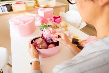 Doğal vücut bakımı, banyo malzemeleri, el yapımı sabun, banyo bombası, ahşap fırça, sünger taşı, sünger taşı, havlu ve dekoratif ayıyla seti hazırlayan bir kadın..