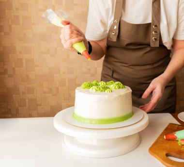 Yeşil kremalı krema koymak ve evde doğum günü pastası süslemek için şekerleme torbası kullanan bir kadın. Ev yapımı yemek pişirme ve pasta süsleme kavramı. Pasta yapan kadın pastacı..