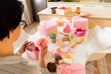 Doğal vücut bakımı, banyo malzemeleri, el yapımı sabun, banyo bombası, ahşap fırça, sünger taşı, sünger taşı, havlu ve dekoratif ayıyla seti hazırlayan bir kadın..