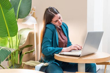 Suitteki iş kadını internet üzerinden bilgisayar kullanarak ve telefonla konuşarak çalışıyor. Serbest çalışan bir kadın dizüstü bilgisayarda geziniyor. Uzaktan çalışma kavramı. Teknoloji ve insanlar. Ağ işi.