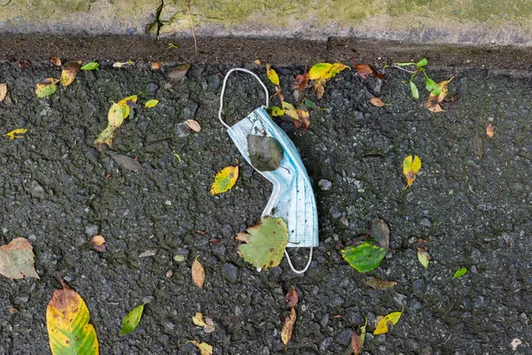 Dirty used medical mask is thrown on the asphalt. Environmental pollution. Not environmentally friendly. The concept of the consequences of the pandemic on the planet.