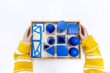Kızların elinin en üst görüntüsü, Montessori okulundaki renkli ahşap geometrik şekiller bulmacasını çözmek ve oynamaktır. Matematiksel geometri kullanma kavramı çocuk eğitimi için kaynak öğrenme kavramı.