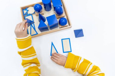 Kızların elinin en üst görüntüsü, Montessori okulundaki renkli ahşap geometrik şekiller bulmacasını çözmek ve oynamaktır. Matematiksel geometri kullanma kavramı çocuk eğitimi için kaynak öğrenme kavramı.